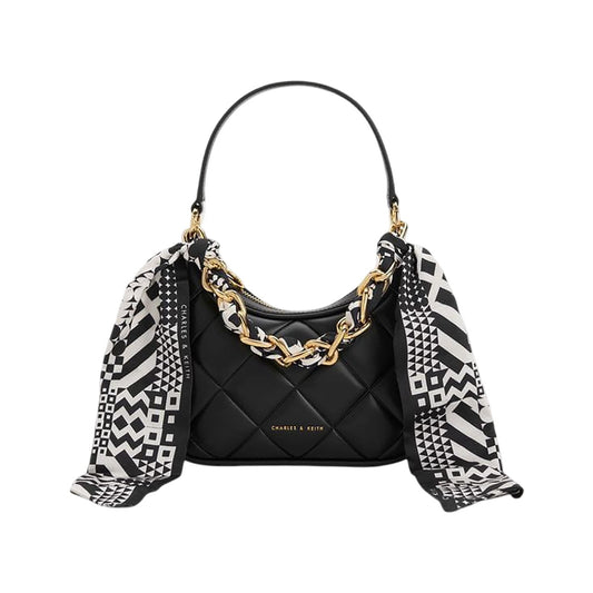 Black quilted handbag with gold chain detail and a black and white patterned scarf draped over it on a white background.