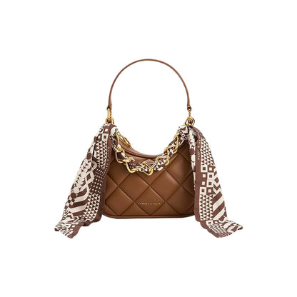 Brown quilted handbag with a patterned scarf draped over it on a white background